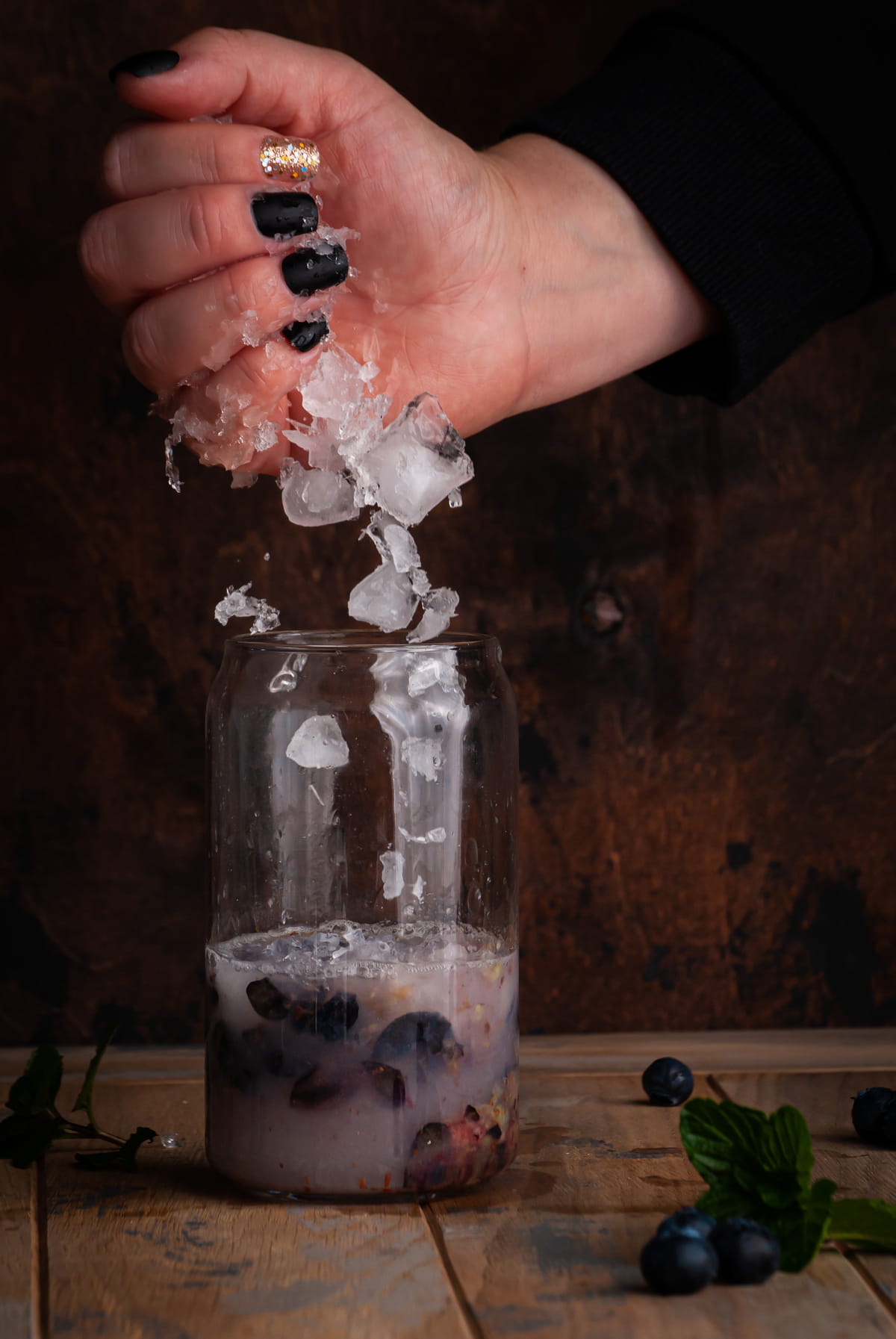 crushed ice being added to a glass with muddled blueberries