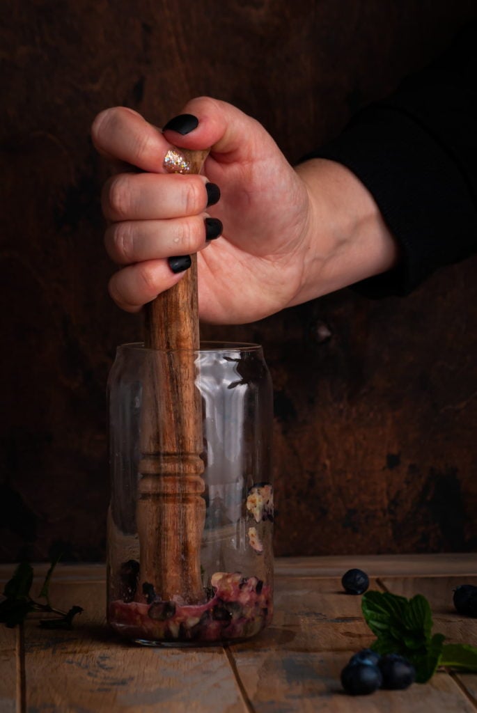 muddling blueberries and mint with a wooden muddler in glass