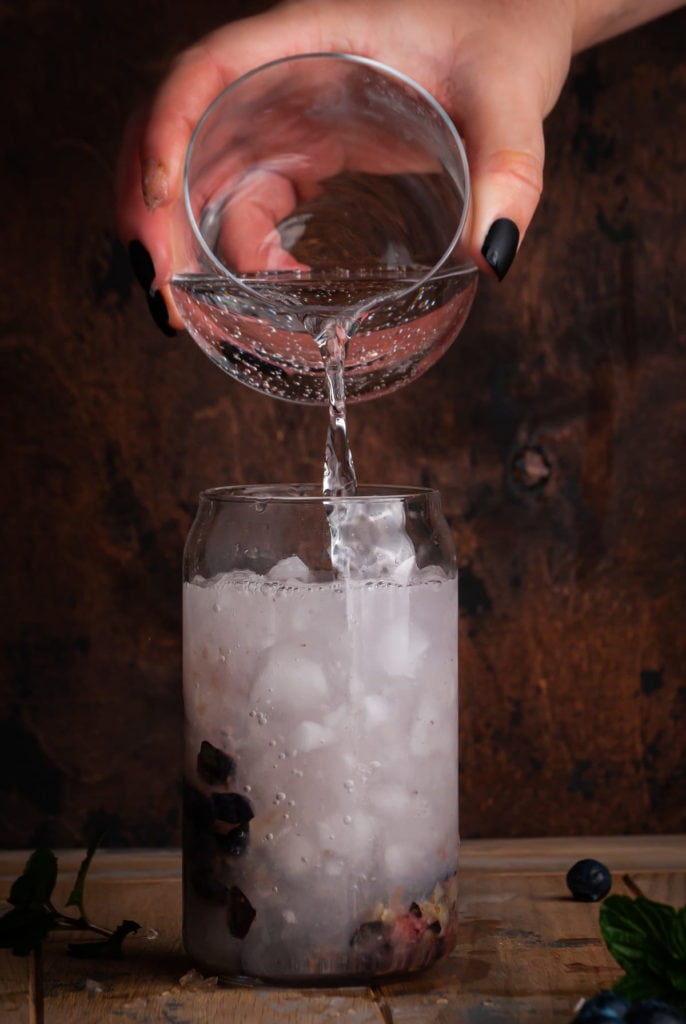 pouring club soda ontop of blueberry gin cocktail to make a blueberry gin fizz