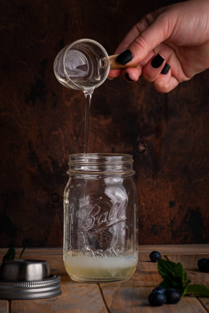 pouring simple syrup into a cocktail shaker with gin