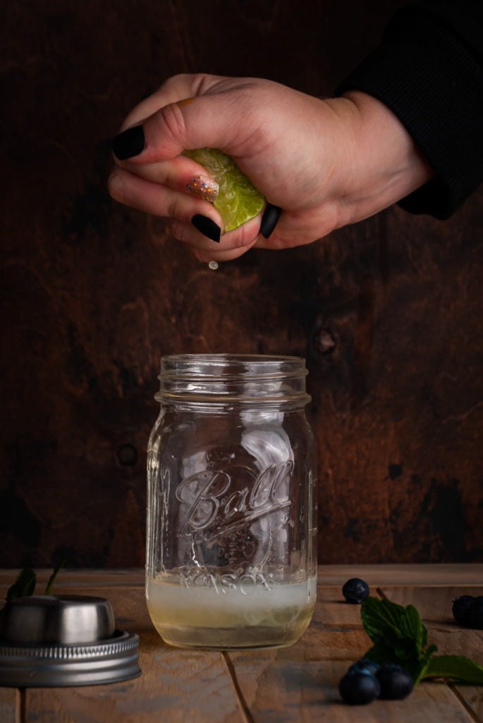 squeexing lime juice into a cocktail shaker