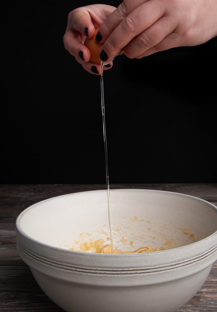 cracking an egg into a large bowl with smashed bananas