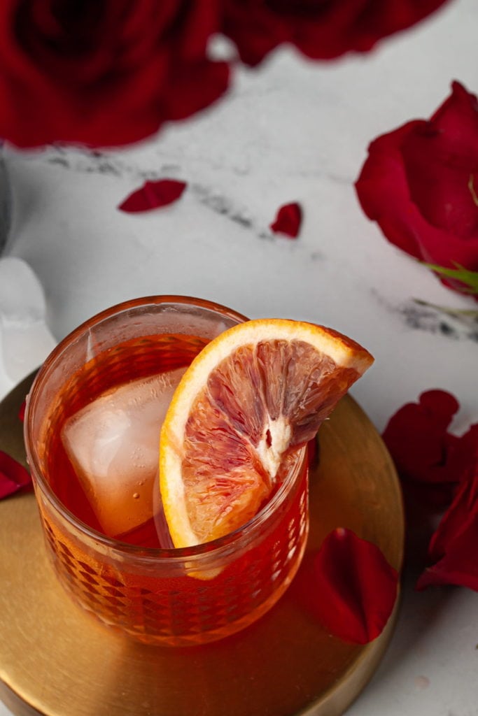 Aperol Negroni with slice of blood orange surrounded by roses