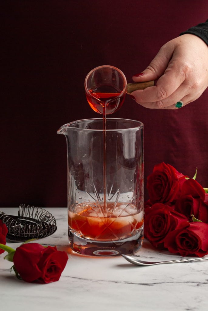 pouring bright red Aperol into a mixing glass