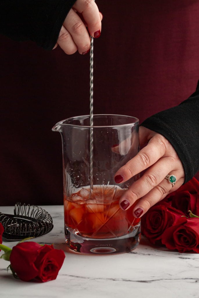 stirring a vibrant red cocktail in a mixing glass