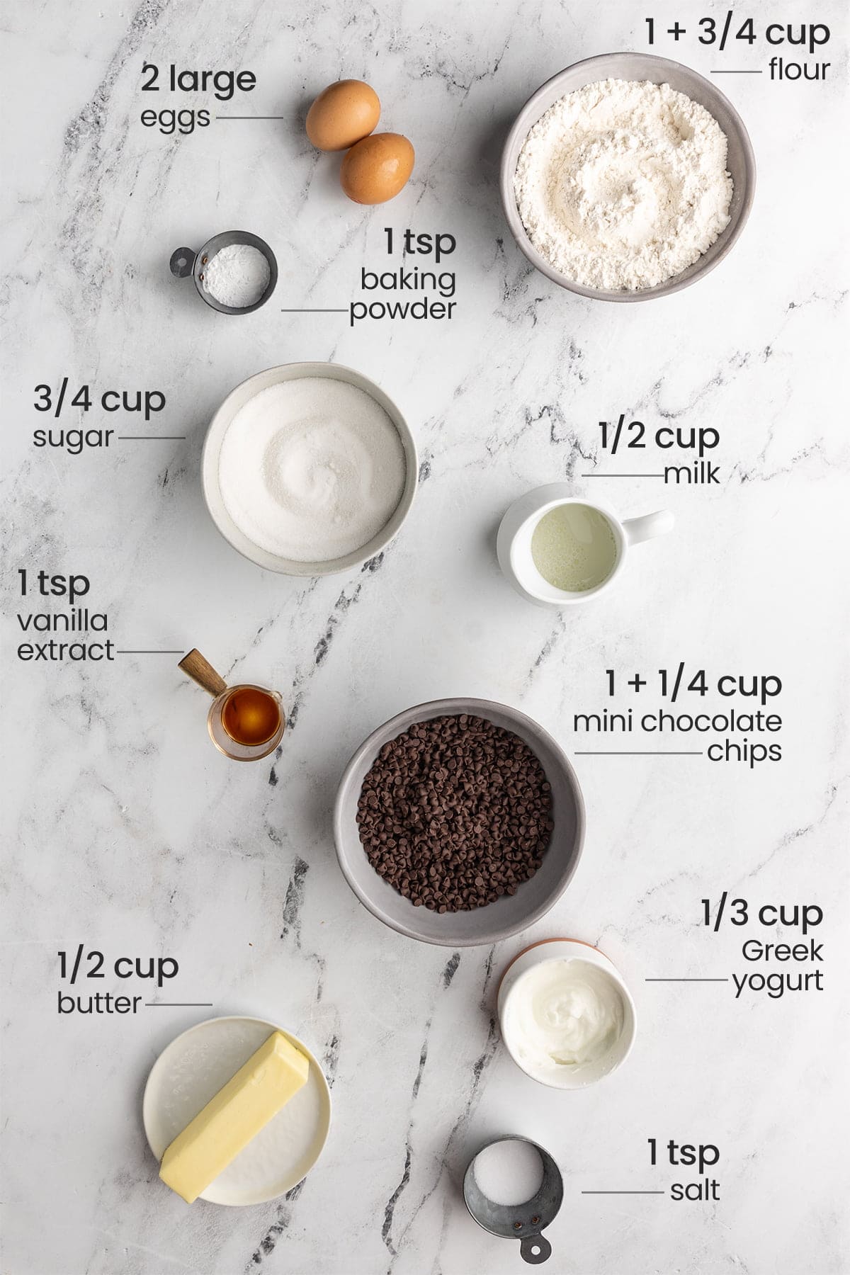 all ingredients for chocolate chip loaf cake - eggs, flour, baking powder, sugar, milk, vanilla extract, mini chocolate chips, Greek yogurt, butter, salt