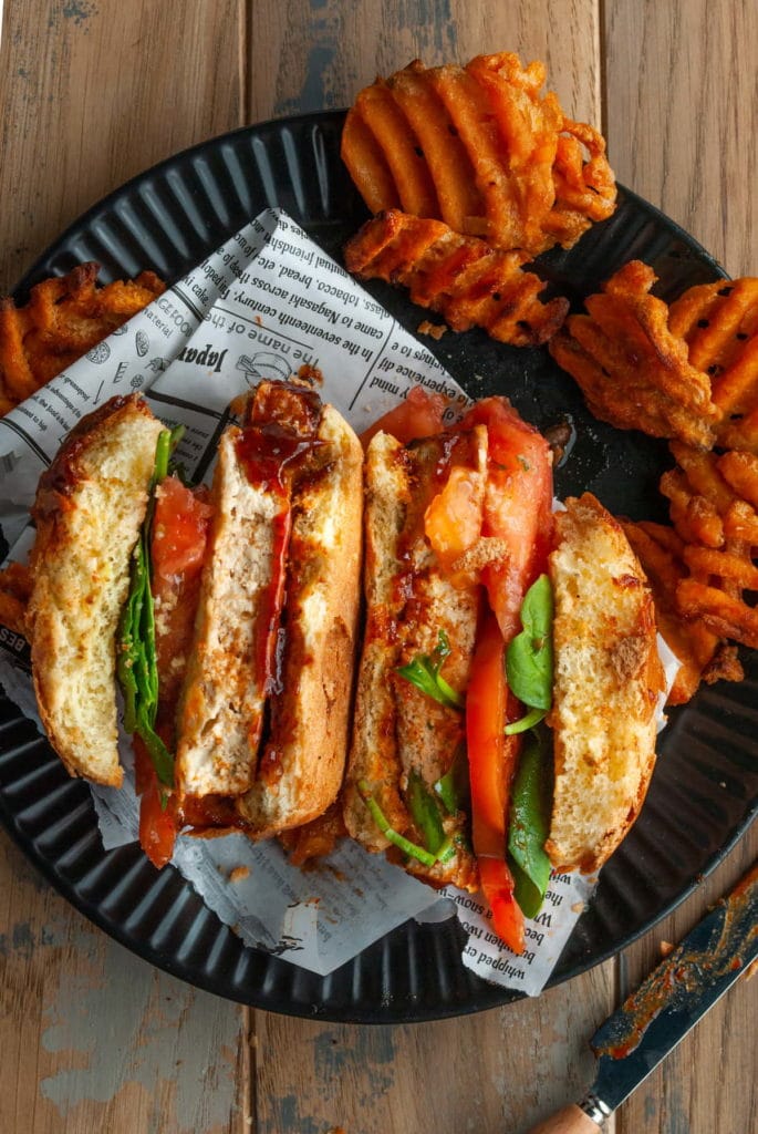 sliced open bbq tofu sandwich laying on its side surrounded by sweet potato fries