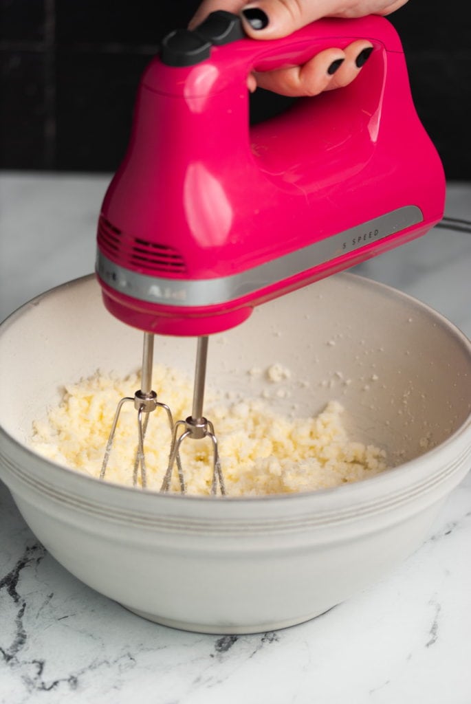 using a pink hand mixer to cream together butter and sugar