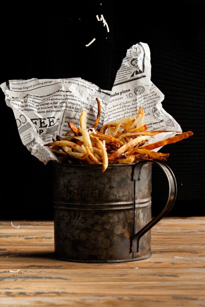 sprinkling parmesan cheese on parmesan truffle fries in a galvanized mug