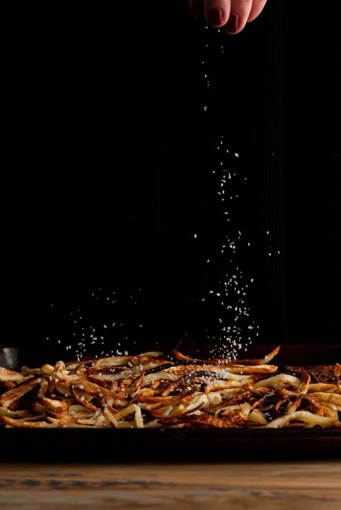 adding salt to parmesan truffle fries