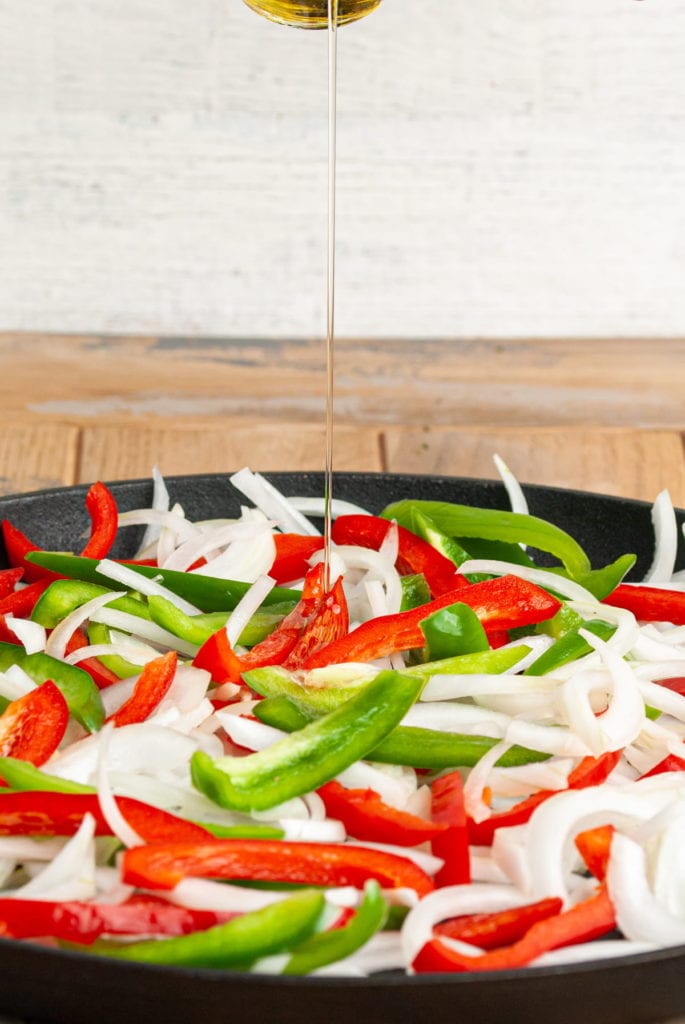 adding olive oil to pepper and onions in cast iron pan