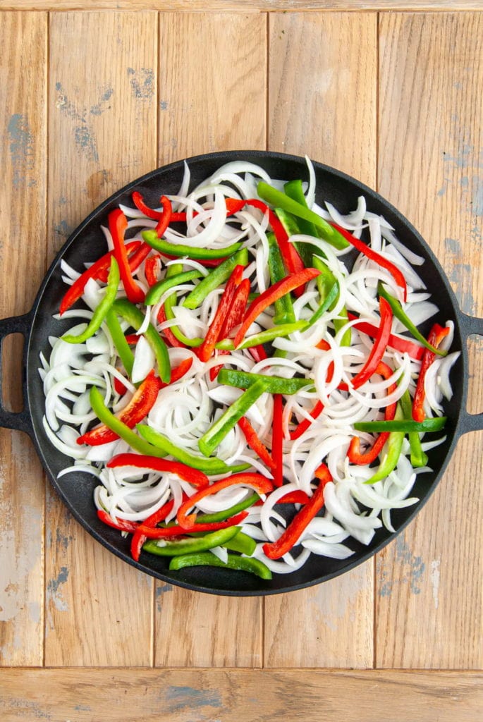 sliced onions, green and red peppers in a cast iron pan
