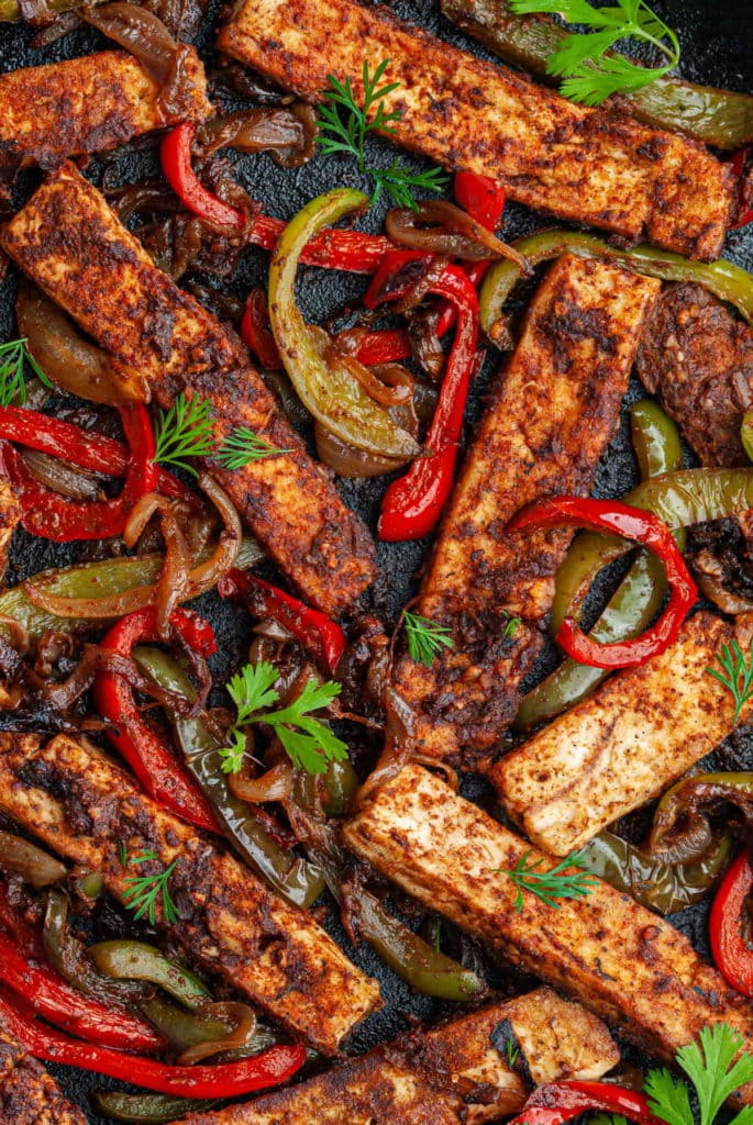 close up of cast iron pan with tofu fajitas with onions and pepper in it