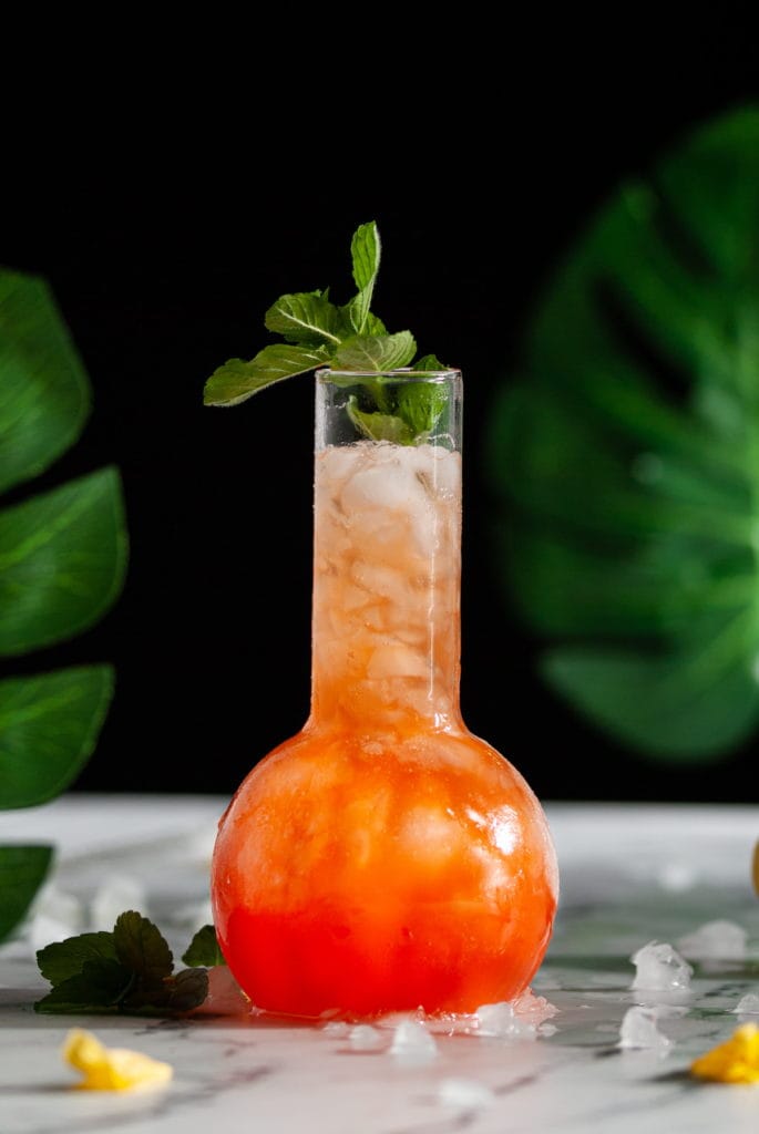 tropical drink in a fun cocktail glass with banana leaves in foreground and background