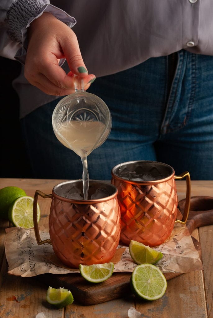 pouring ginger beer from a small glass pitcher into a copper mug