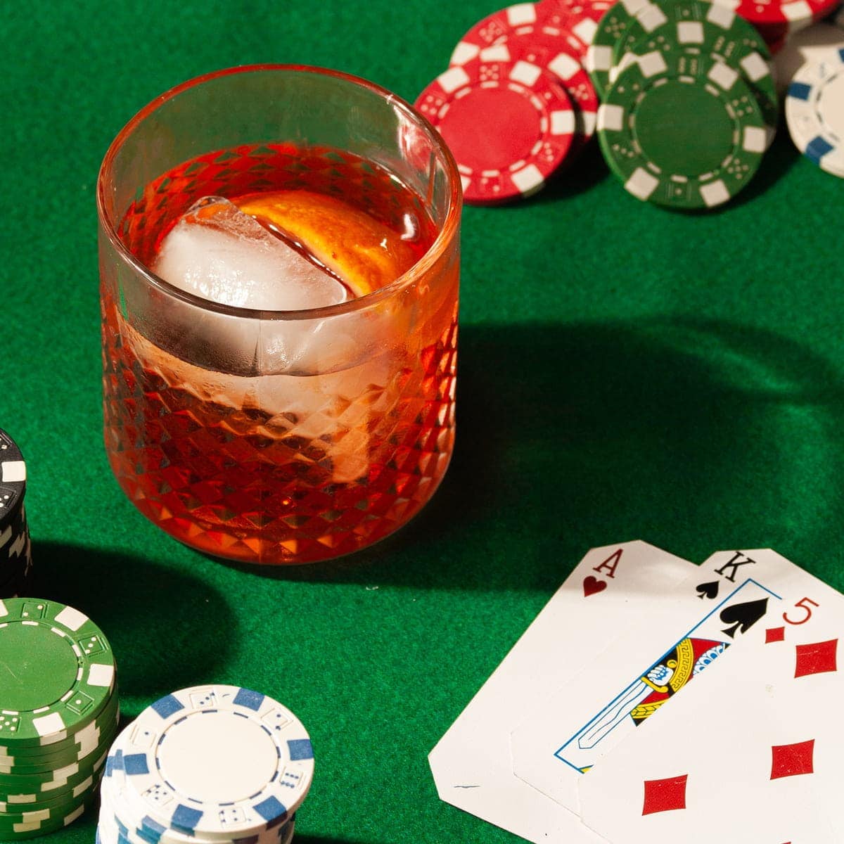 Aperol Old Fashioned on green felt surrounded by poker chips