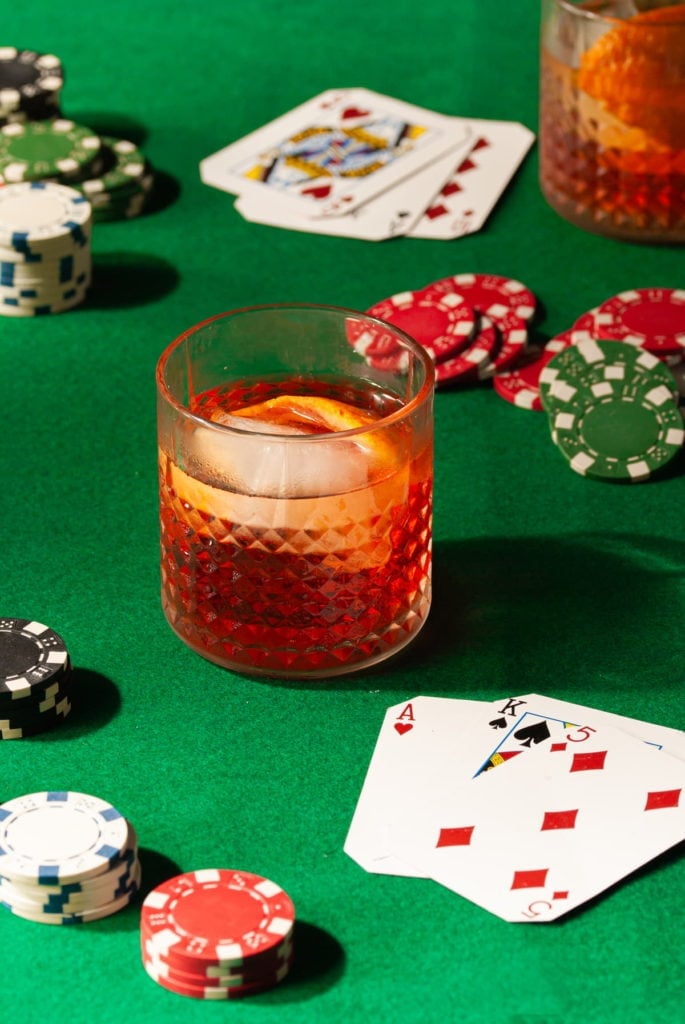 aperol old fashioned with whiskey ice surrounded by playing cards and poker chips