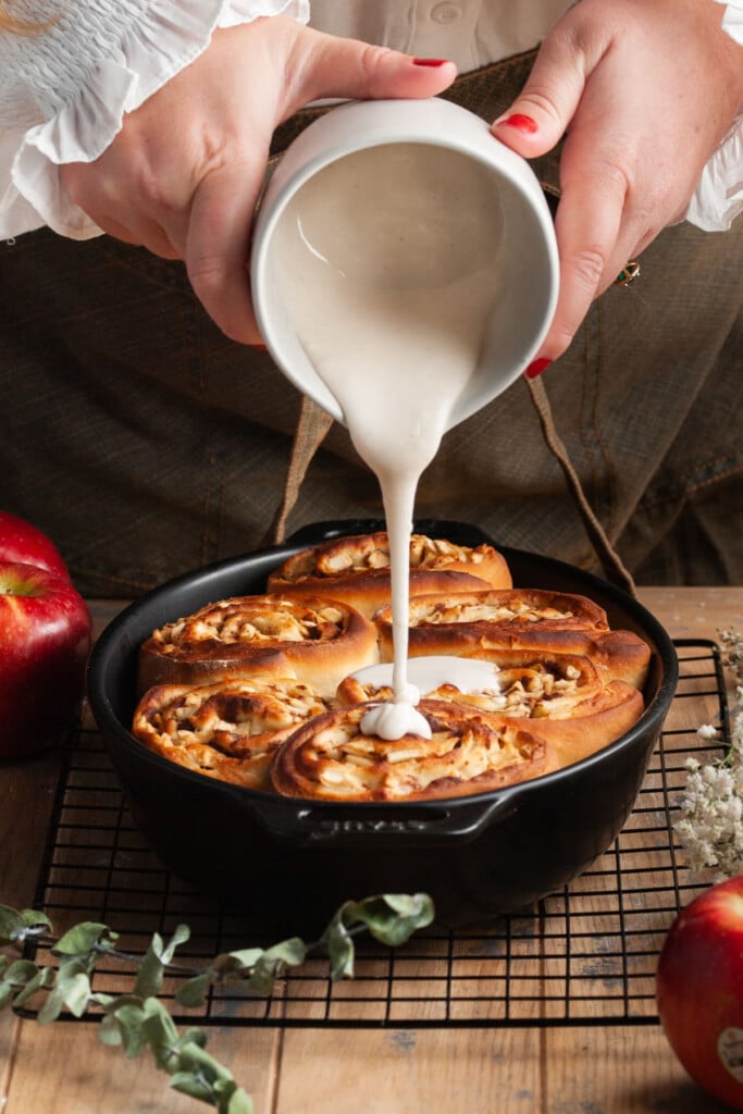 Pouring icing over apple pie filled cinnamon rolls.