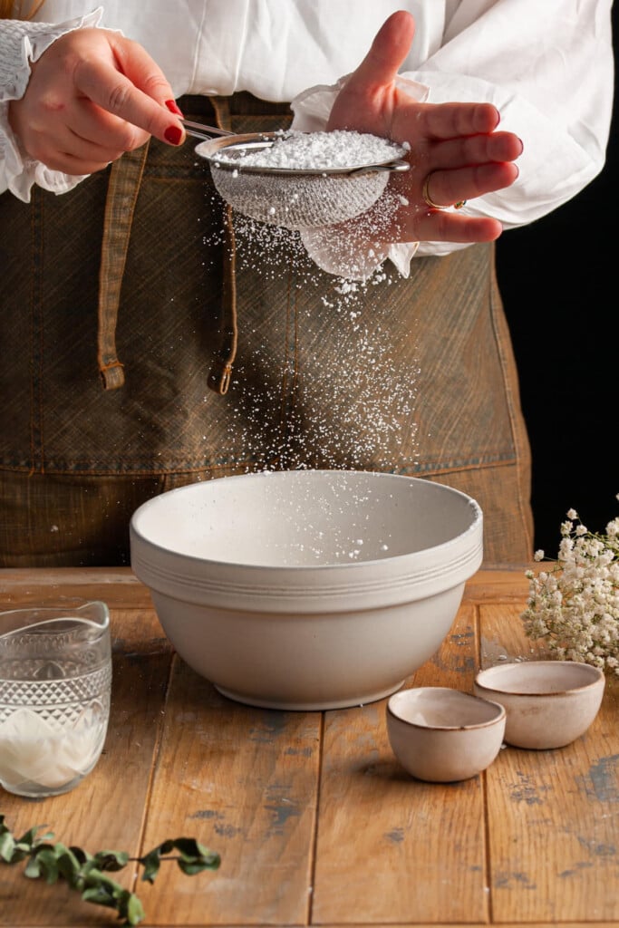 Sifting powdered sugar into a bowl to make simple icing for cinnamon buns.