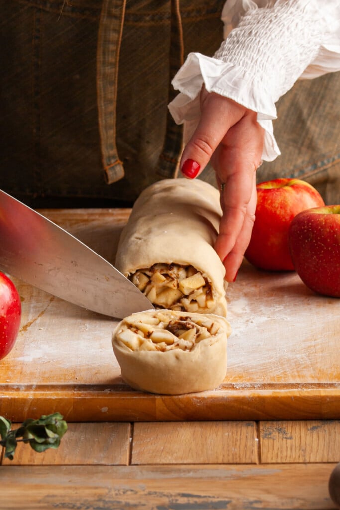 Slicing through apple pie filling rolled up in dough to form individual cinnamon rolls.