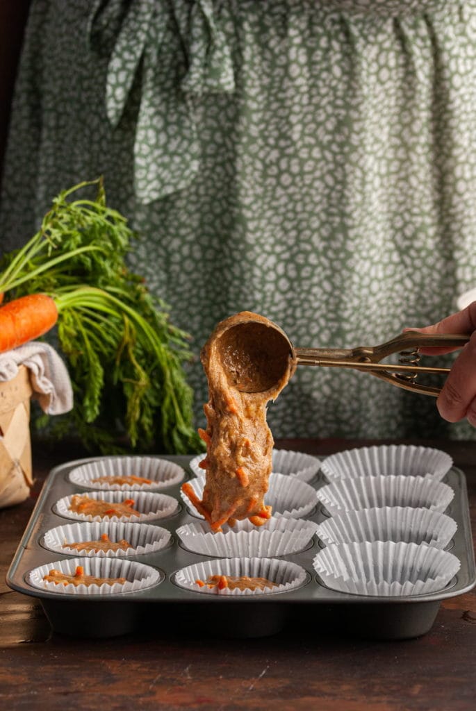 adding banana carrot muffin batter to a lined muffin tin