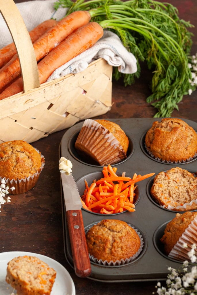 banana carrot muffins in muffin tin with knife with butter on it