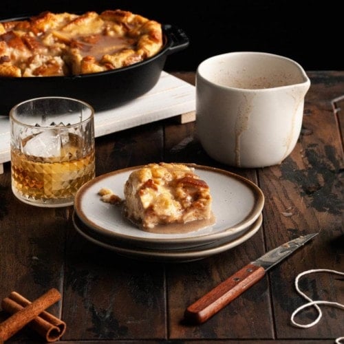 slice of bread pudding next to a glass of bourbon