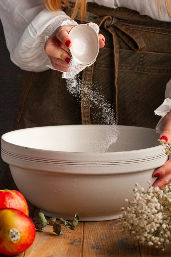 adding sugar to a large mixing bowl to make cinnamon rolls