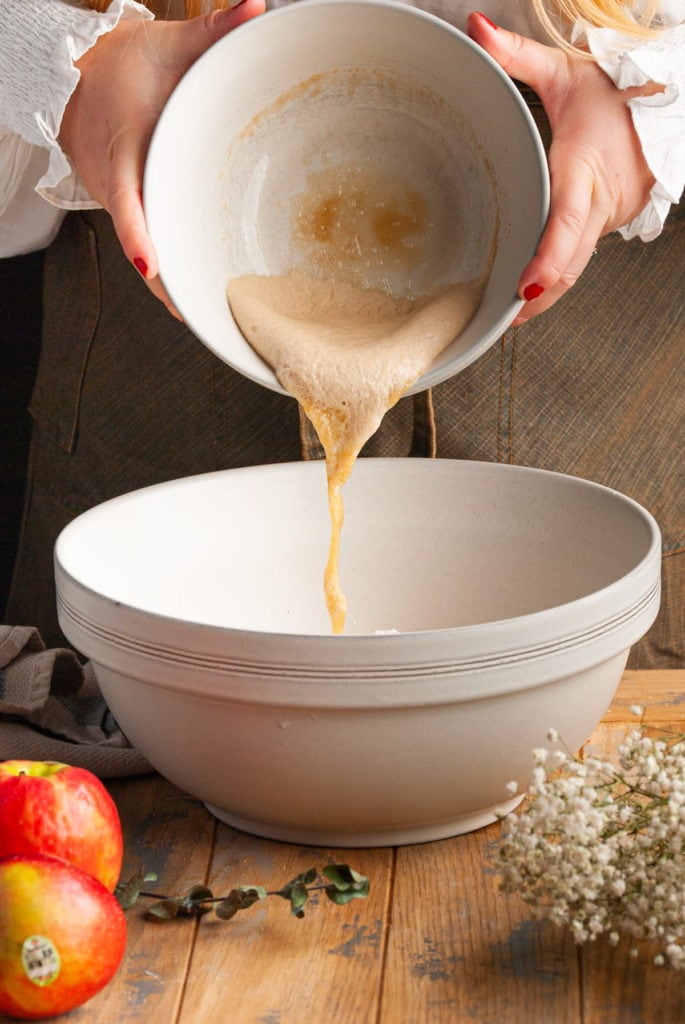 adding activated yeast mixture to mixing bowl with other cinnamon roll ingredients