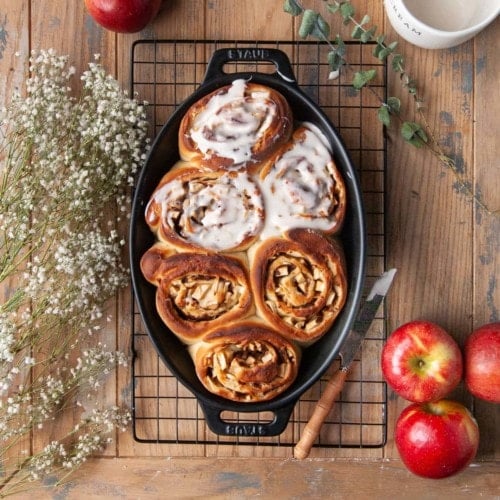 oval baking dish with 6 cinnamon rolls in it, half with icing half without