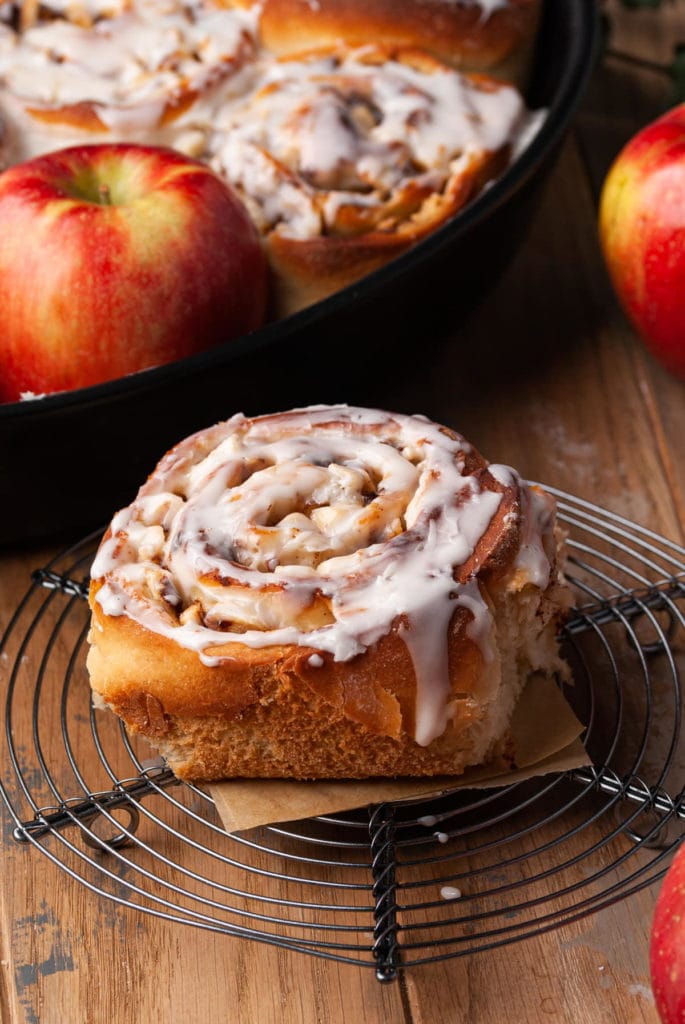 one cinnamon roll on a cooling rack with icing dripping off the side