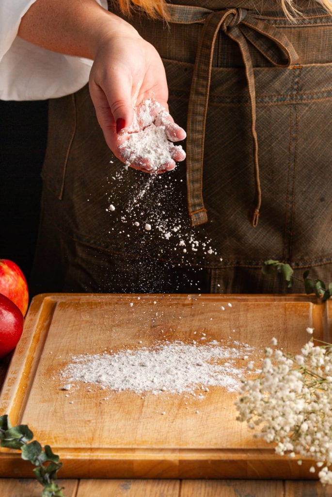 adding flour to the surface of a cutting board to knead dough out on