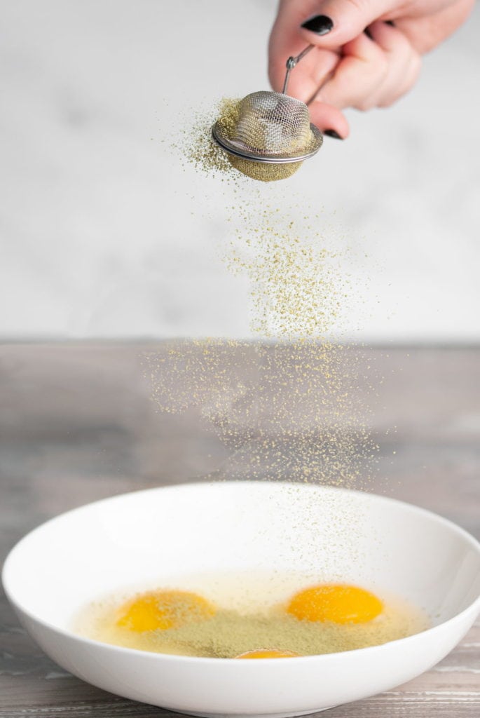 adding matcha powder to a bowl with eggs to make a matcha egg wash