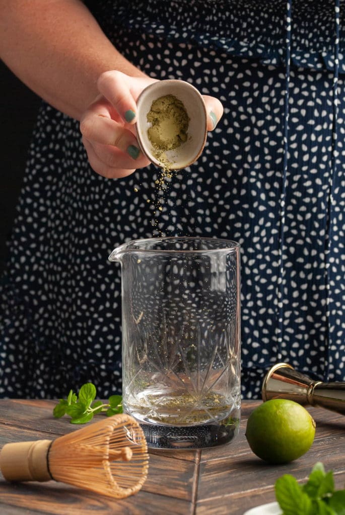 Adding matcha powder to a mixing glass with white rum.