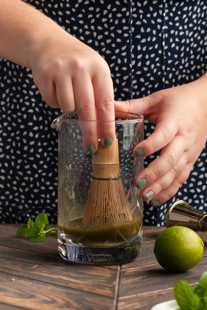 using a matcha whisk to stir matcha and rum together in a mixing glass