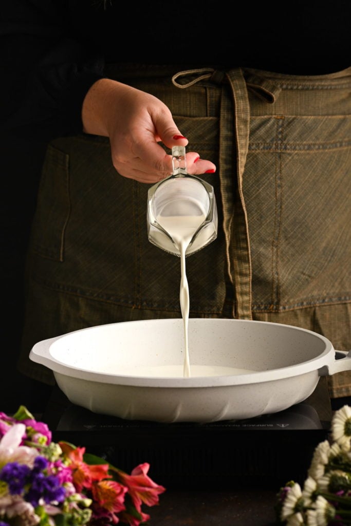 adding cream to a shallow pan to make brandy sauce