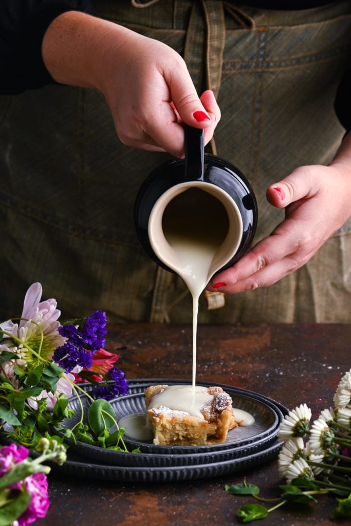 pouring brandy sauce over a slice of bread pudding