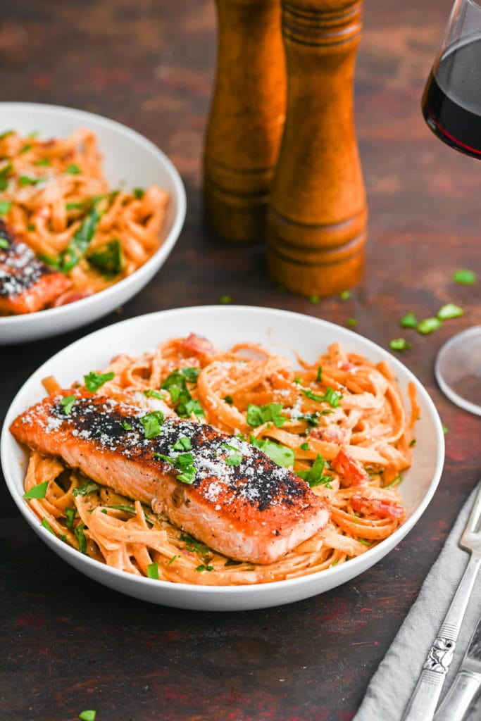Two bowls of cajun salmon pasta with salt and pepper shaker and a glass of red wine