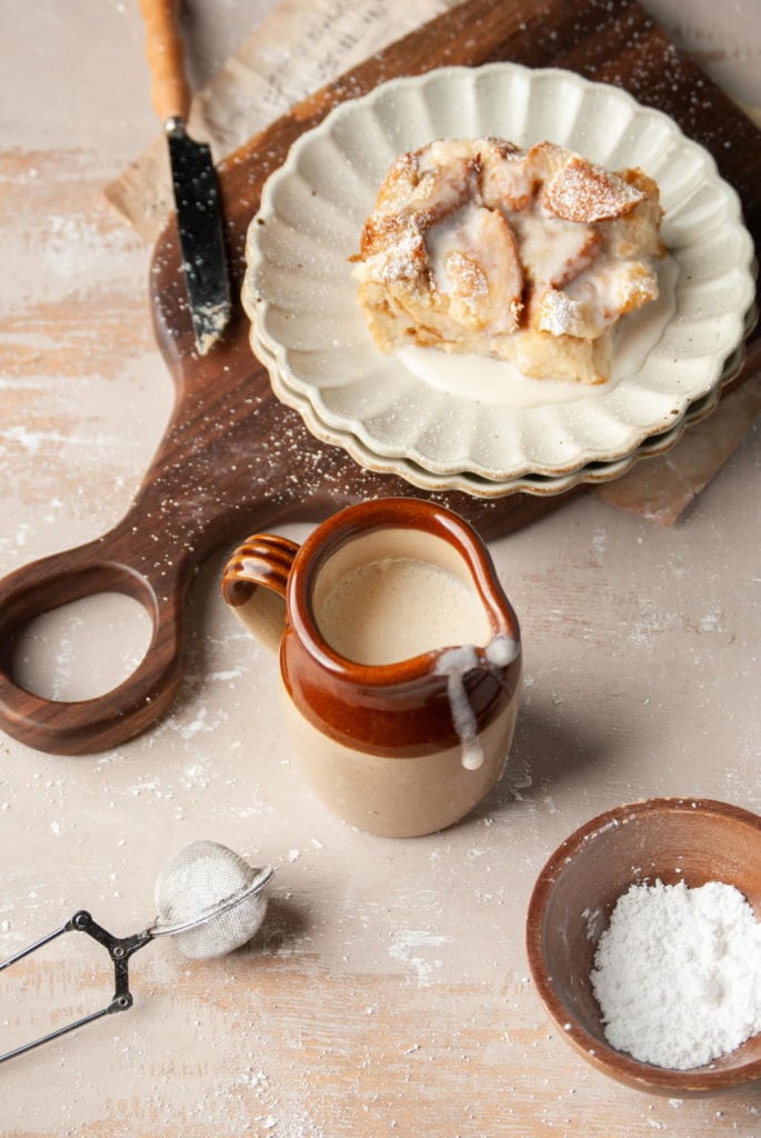 vanilla sauce in creamer pitcher with slice of bread pudding behind it