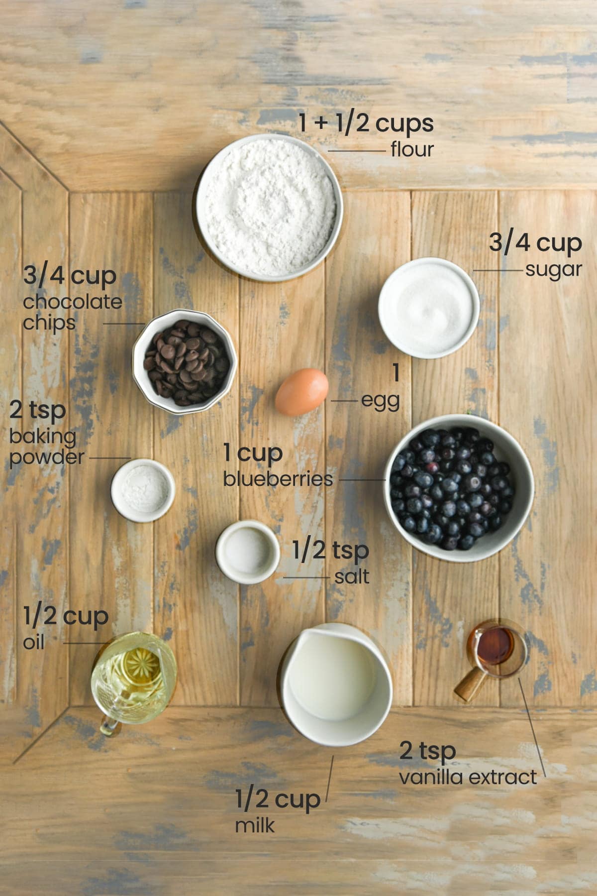 ingredients for blueberry chocolate chip muffins - flour, chocolate chips. sugar, egg, salt, baking powder, blueberries, oil, milk, and vanilla extract