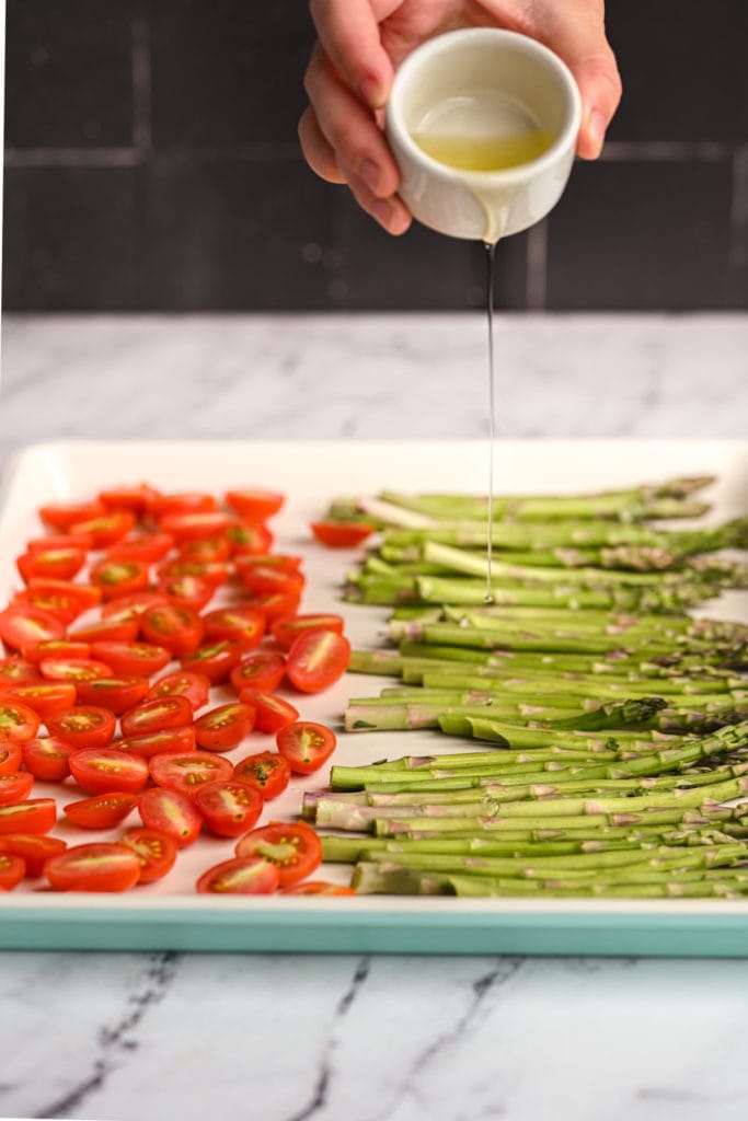adding olive oil to roast tomatoes and asparagus
