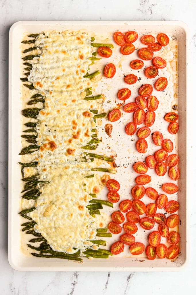 roasted asparagus and grape tomatoes with melted and browned cheese on top of the asparagus