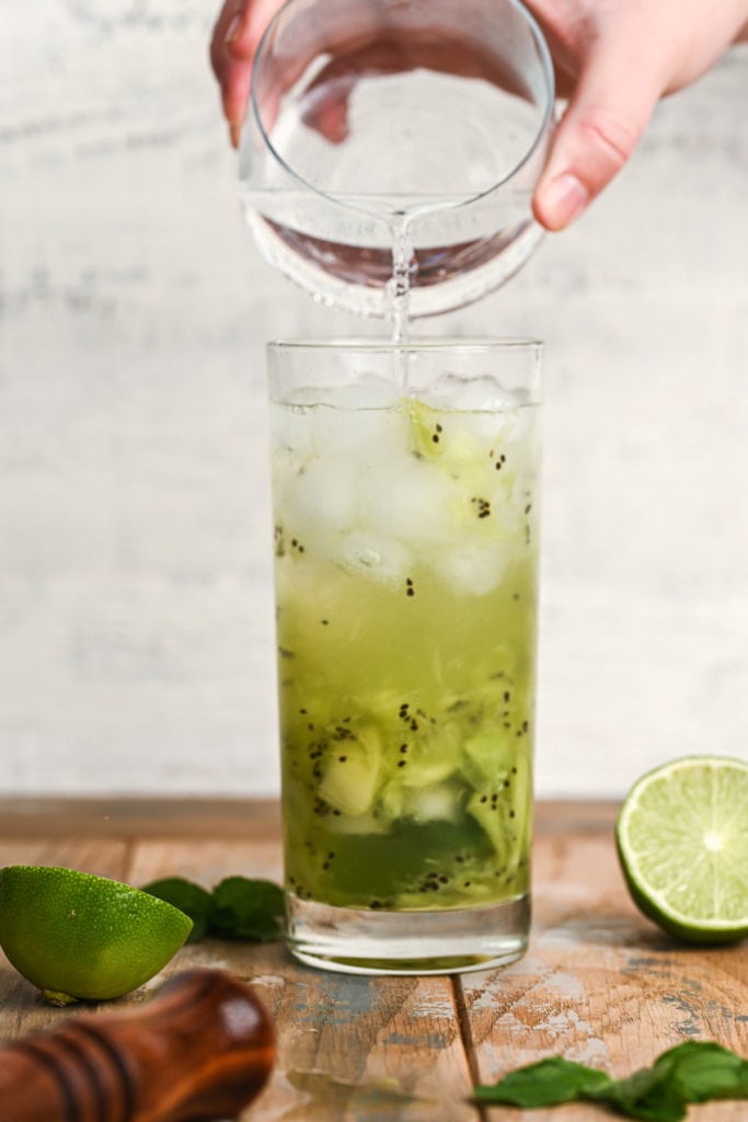 adding club soda to top kiwi mojito with bubbles