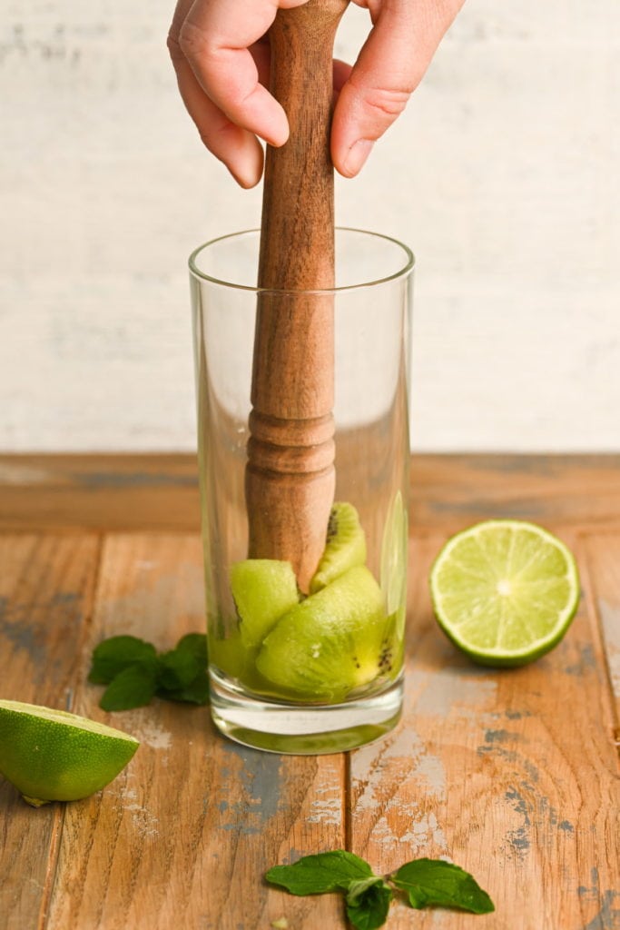 using a muddler to muddle together kiwi and mint