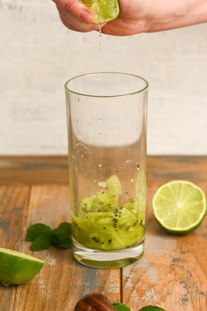 squeezing fresh lime juice into glass with muddled kiwi and mint