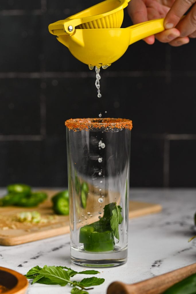 using a handheld citrus juicer to add lime juice to spicy mojito