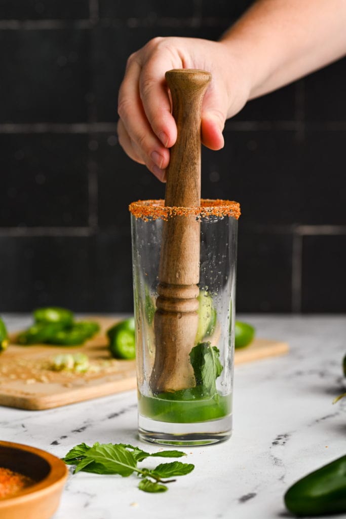 using a wooden muddler to crush jalapenos and mint to extract flavor