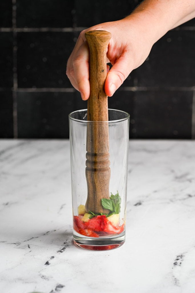 using a muddler to crush mint strawberry and pineapple in a highball glass