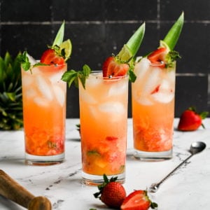 3 fruity mojitos garnished with a pineapple stem, strawberry, lime and mint