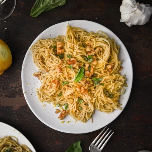 small plate of tahini pasta with toasted walnuts and garnished with chopped basil